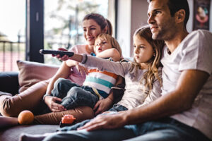 A mom, dad, pre-teen daughter and toddler son are all on the couch watching TV together