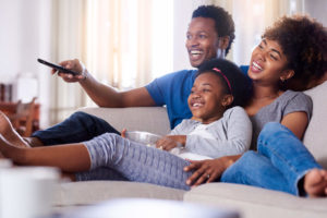 Dad, mom, and daughter cuddling on couch together watching TV in living room