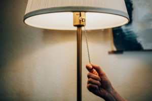 A hand pulling the pull chain on a lighted lamp