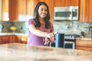 Woman in a kitchen tapping a smart speaker