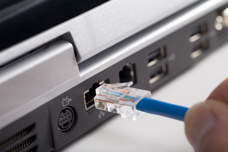 Fingers plugging ethernet cable into back of laptop