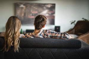 Couple sitting on living room couch watching cable TV on big screen