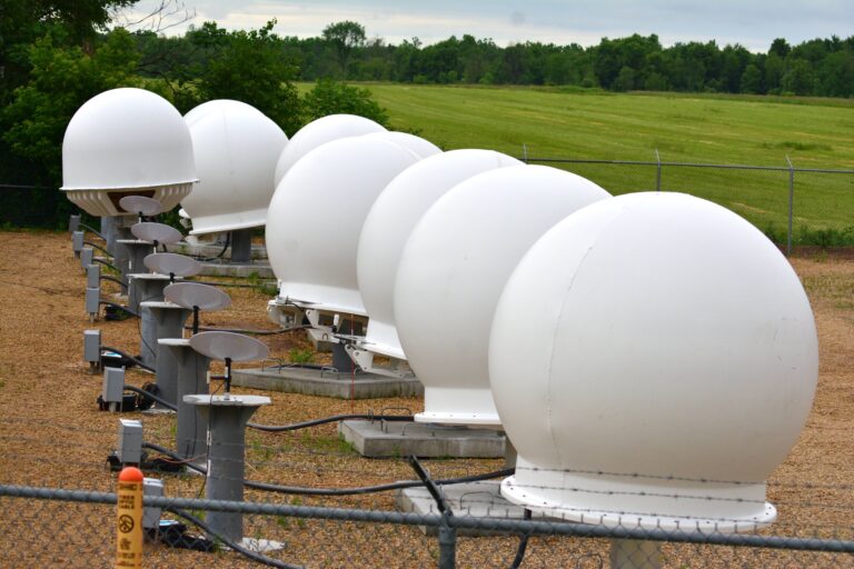 A row of about seven Starlink ground terminals, each one is a white sphere with a skirt on the bottom and sits on a concrete pad